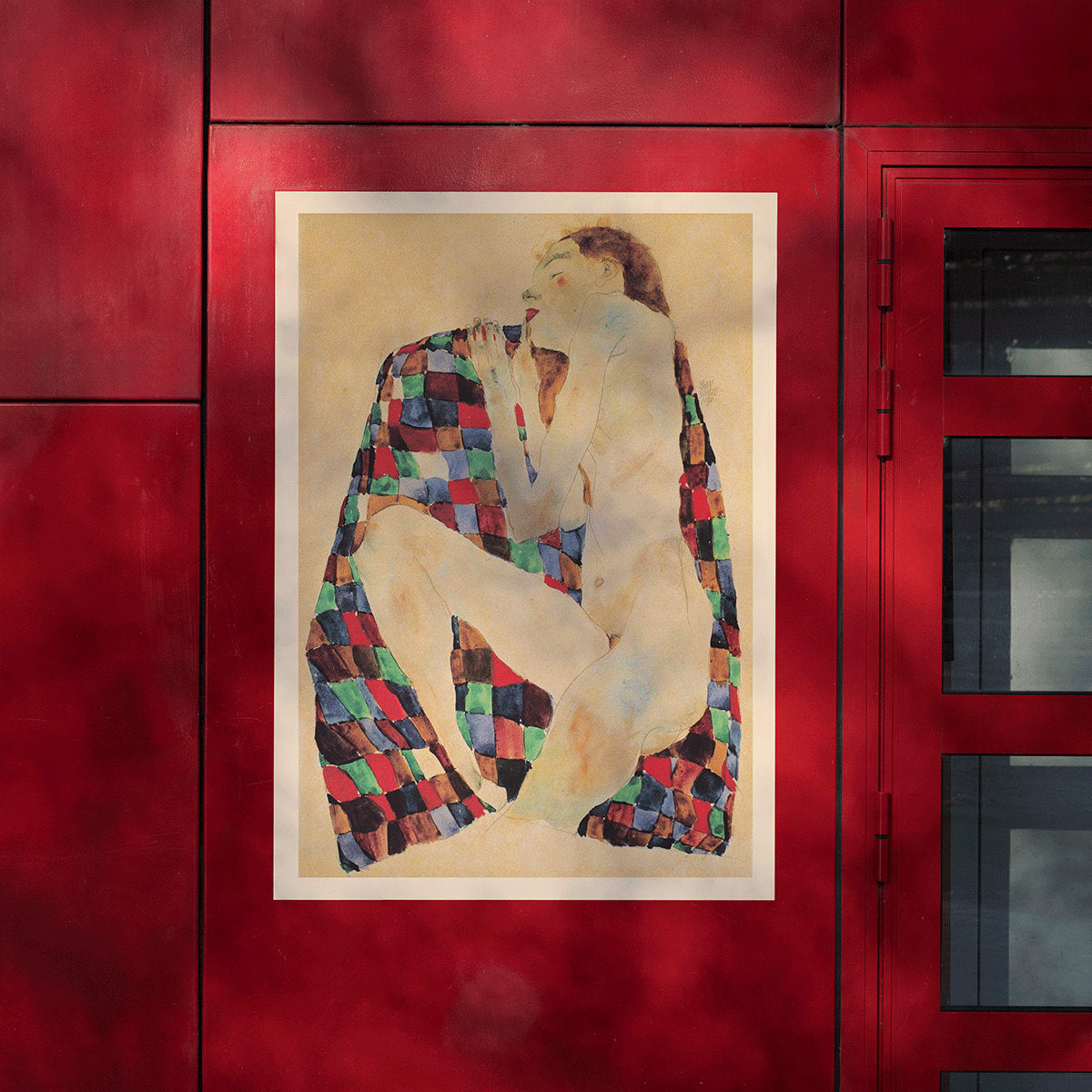 Female Nude on Checkered Cloth by Egon Schiele showing a nude woman sitting on a colorful patterned fabric poster, framed and displayed in modern living room decor