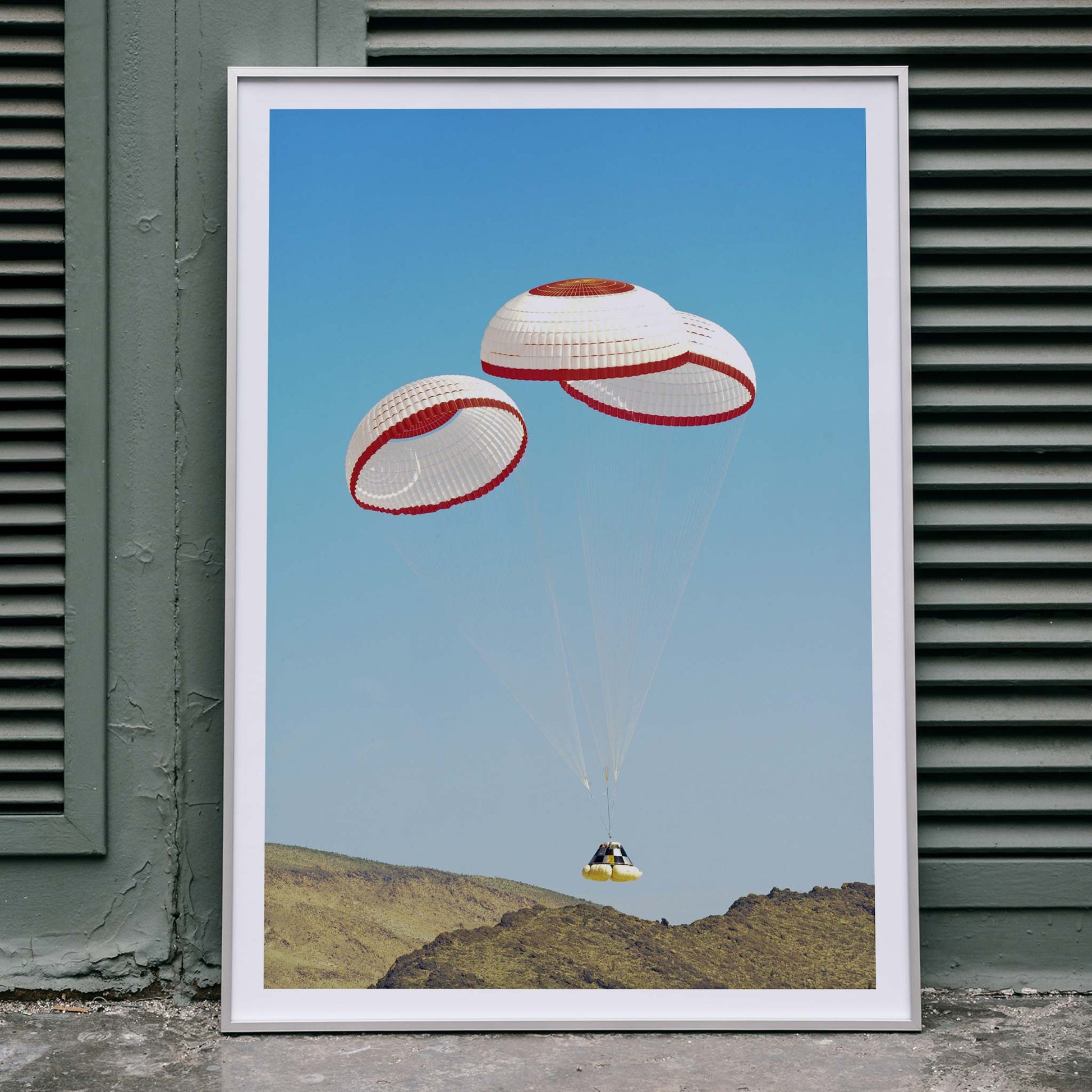 CST-100 crew capsule landing with three parachutes over desert landscape by NASA and The Boeing Company poster artwork, framed and displayed in home decor