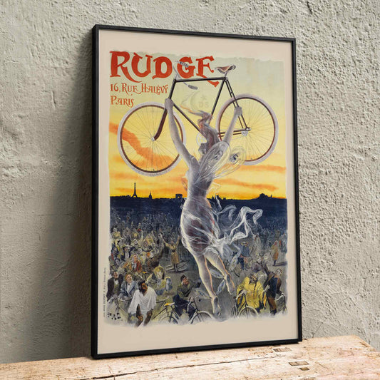 Vintage bicycle poster by Jean de Paleologue showing a triumphant figure and a woman holding a bicycle above a crowd at sunset for Rudge bicycle brand, framed and displayed in home decor